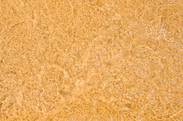 transparent water texture. golden sand is visible through the clear sea water. Abstract Background of Beach Ocean Water