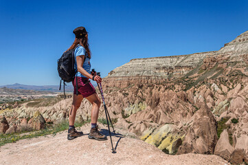 A woman with a backpack stands on a high mountain in Cappadocia and looks at the multi-colored rocks. Turkey