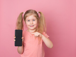 Smiling little girl showing blank screen of new popular mobile phone on pink background.