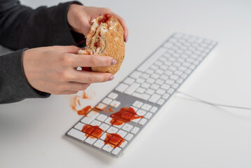 A faceless woman is eating a burger and dripping ketchup on the keyboard