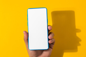 man hand holding blue smartphone with blank screen, isolated on yellow background