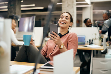 Young businesswoman laughing while using smart phone on coffee break at corporate office.