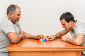 Teenager son and senior father sitting in home and playing with flexible toy the pop It fidget. Poppit new fidget toy, popular with kids, and people with special needs, help them to concentrate.
