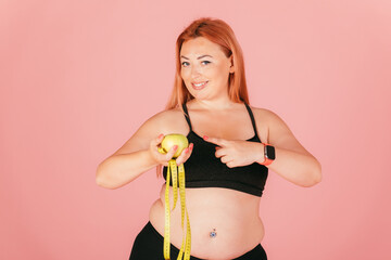 Portrait of beautiful oversized woman wearing sports outfit holding apple