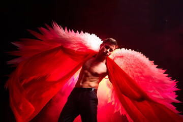 Handsome young athletic man with a bare torso who looks like an angel with white wings. Model...
