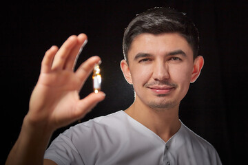 Obraz premium A young man who is a medical doctor in a white uniform poses against a black background in the studio with an ampoule in his hand