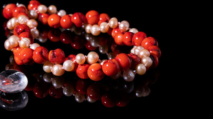 Twisted shiny red coral and iridescent  pearl necklaces on a black  background. Isolated coral jewelry, pearl jewelry with reflection. 