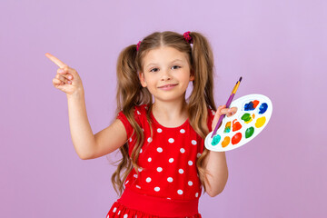 A girl in a red dress with a palette and a brush in her hands points her finger to the side.