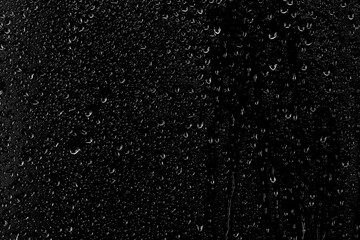 Drops of water flow down the surface of the clear glass on a black background. Texture for creativity.	
