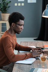 African young man sitting at the table and using computer for his study at home