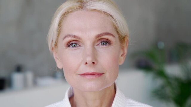 Closeup portrait of attractive middle aged blond woman wearing bathrobe with natural makeup looking at camera. Advertising of perfect antiage skin care products, hotel spa services concept.