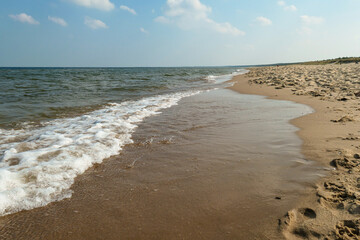 The coastal line of a sandy beach by the Baltic Sea on Sobieszewo island, Poland. The sea is gently waving. A bit of overcast. Solitude and serenity