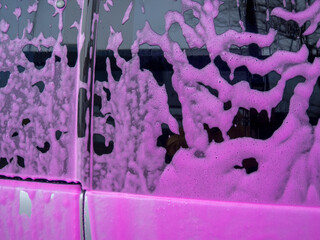 Covered auto with pink foam at a self-service car wash. car wash with a spray of magenta soap from...