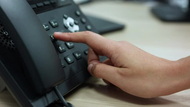 slow motion scene of employee woman hand press number to dial and touching handset of telephone on desk for contact customer or receiving call for communication and helpdesk woking concept