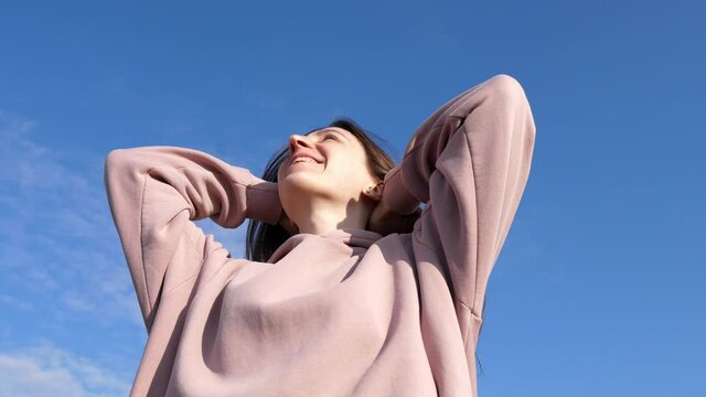Happy young woman enjoys life and the blue sky above her head. Dream fulfillment portrait against sky background.