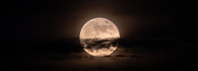 horizontal panoramic image of the full moon slightly obscured by clouds during the night - obrazy, fototapety, plakaty