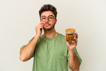 Young caucasian man holding an almond jar isolated on white background with fingers on lips keeping a secret.