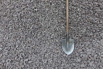 An old steel shovel with a wooden handle rests on a pile of gray granite gravel. There are small spots of dirt. Background. Texture.