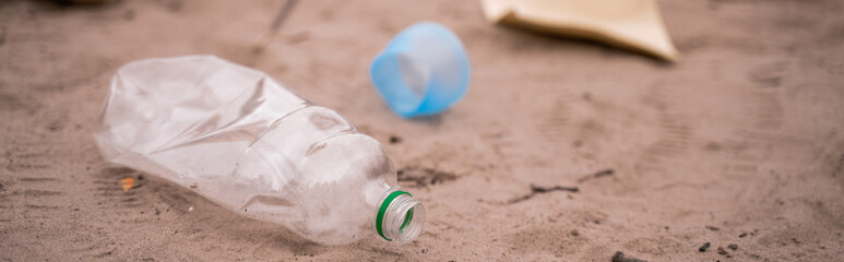 plastic bottle near trash on blurred sand, banner