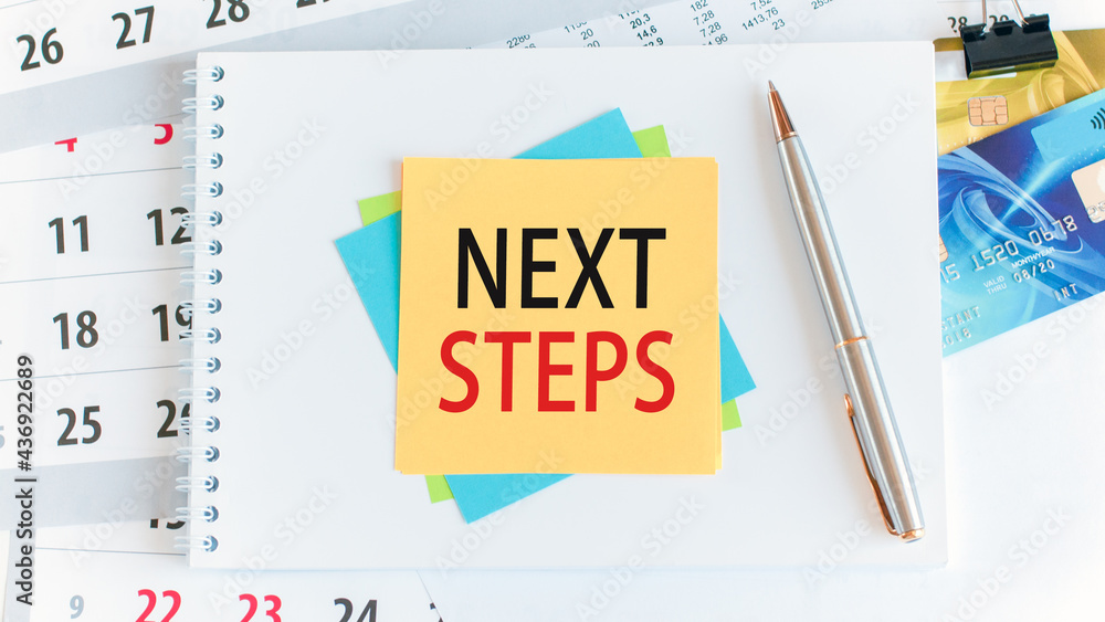 Poster next steps, the text is written on yellow paper lying on a white notepad on the desktop of an office