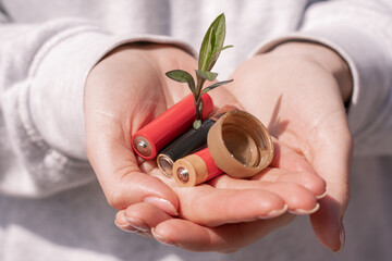 cropped view of woman holding batteries, plastic bottle cap and green plant in hands