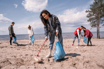 smiling young woman holding trash bag and collecting rubbish on sand near group of volunteers © LIGHTFIELD STUDIOS