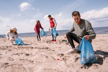 young man holding trash bag and collecting rubbish on sand near group of volunteers © LIGHTFIELD STUDIOS
