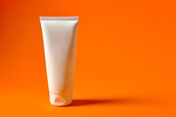 White tube with cream on an orange background, place for an inscription, side view