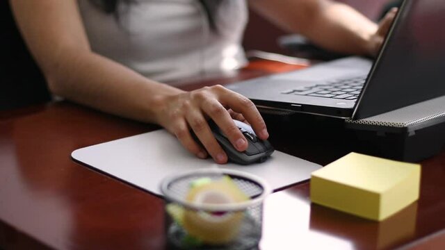 Close up of a young woman in her office. She is working and typing on her computer, she is using the mouse.