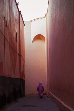 local woman in a pink dress walks along the narrow streets of the classic pink Marakesh in the old city center