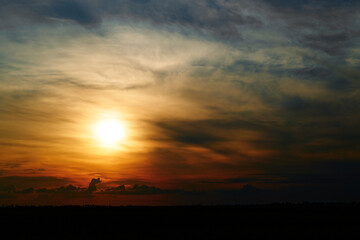 beautiful sunset sky, bright sun and dark silhouette of clouds as a background