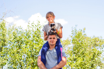 Defocused brother riding sister on back. Portrait of happy girl on man shoulders, piggyback. Girl...
