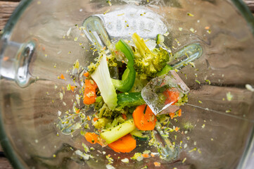 In the photo you see a mix of fresh vegetables. Vegetables, cut into pieces, are randomly arranged on a glass salad bowl. You also see juice splashing. Abstraction. Light background. View from above.