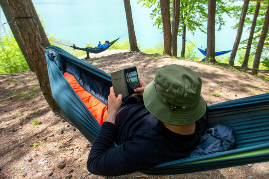 Man sitting in hammock on the edge of a lake and taking pictures with his phone