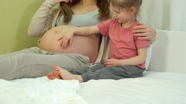 Preschooler daughter stroking mom pregnant belly. Second pregnancy of a woman. Pregnant and todler child daughter at home. concept of pregnancy, mother during second pregnancy. Motherhood family