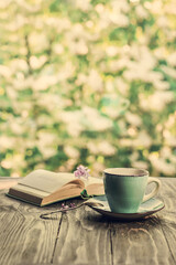 Morning coffee. Cup of coffee and an open book on a wooden table in the garden. Life style.