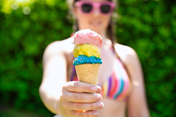 young female in rainbow colored swimwear giving ice cream, two colorful different flavors ice cream...