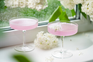 Fresh pink non alcoholic cocktail in glass with lilac flowers against window background.