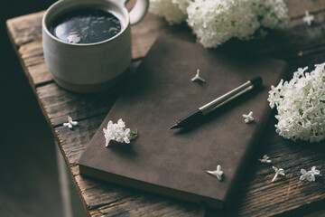 Spring composition with cup of coffee, old book and white lilac beautiful bouquet. Concept of spring and comfort
