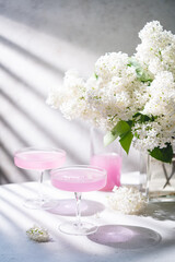 Fresh pink non alcoholic cocktail in glass with lilac flowers against white background.