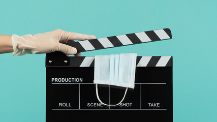 black Clapper board or movie slate with face mask in hand that wear medical gloves on  mint green...