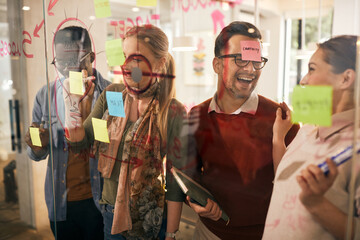 Cheerful business colleagues having fun while creating mind map on glass wall in the office.