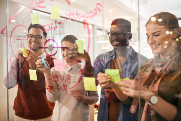 Happy business team cooperating while making mind map on glass wall in the office.