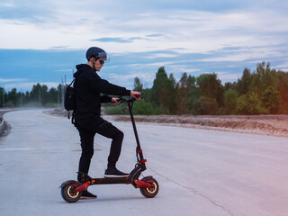 A young man wearing a helmet rides a powerful modern electric scooter on an unfinished road....