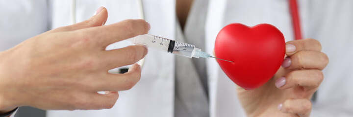 Doctor injecting medicine into red toy heart closeup
