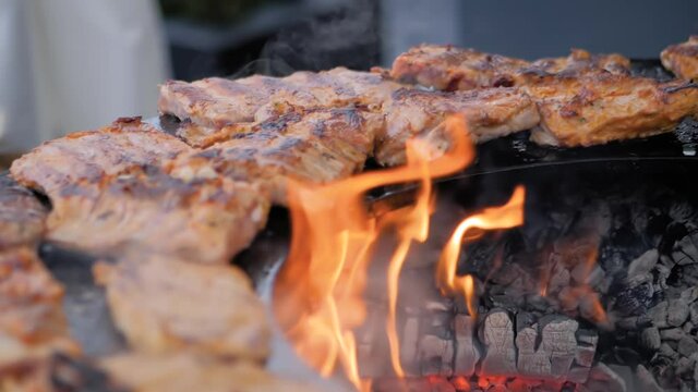 Process of cooking fresh juicy meat steaks on brazier with hot flame at summer local food market - slow motion, close up. Outdoor cooking, gastronomy, cookery, street food concept