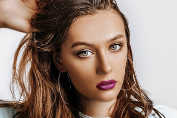 Naklejka premium Beautiful young brunette girl with green eyes with long hair with fashion makeup with purple lips on an isolated gray background. The woman seriously looking at the camera. Kind cute model