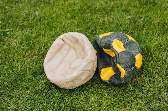 A pair of deflated football old multi-colored balls lie on the green grass of the sports field. Photo of the match. The end of a football player's career.