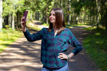 Young girl is taking a selfie on her mobile smartphone camera on the background of a forest landscape