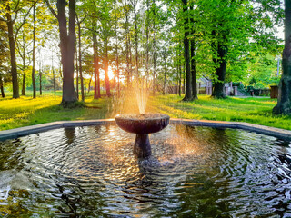 Park dworski w Iłowej. Parkowa fontanna oświetlona promieniami zachodzącego słońca.